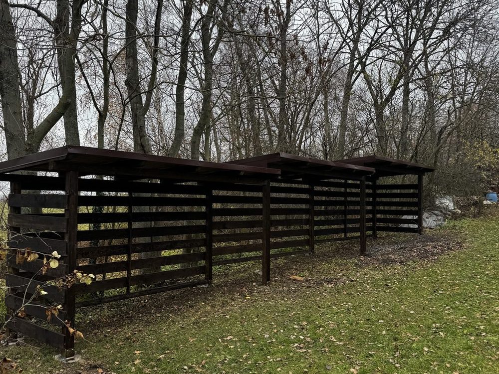 Dlouhý tmavý dřevník z vodorovných prken na okraji zahrady