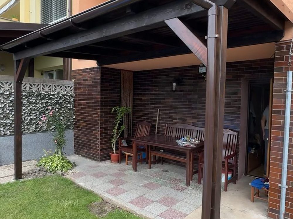 Tmavá dřevěná pergola s palubkovým záklopem nad posezením u domu